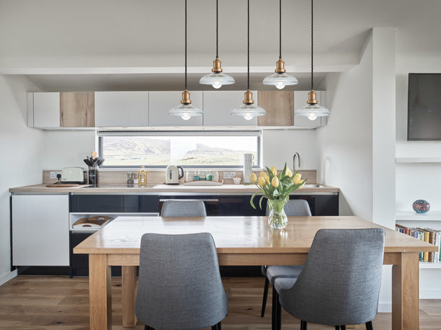 A modern kitchen with a five-wire cluster chandelier light with glass pendants hanging over a dining table 