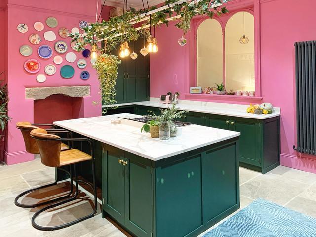 A pink and green kitchen decorated with plates on the wall and hanging lights