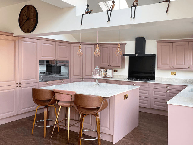 A kitchen with pink cabinets and hanging pendants