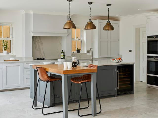 Three brass dome pendants hanging over an island in a white kitchen 
