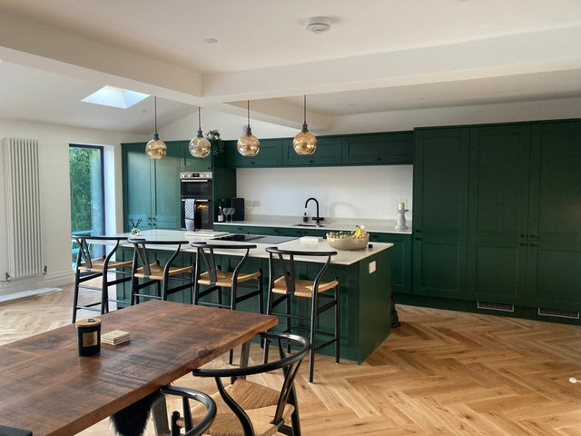  A modern kitchen with dark green cabinets, wooden floors and glass pendant globe lighting