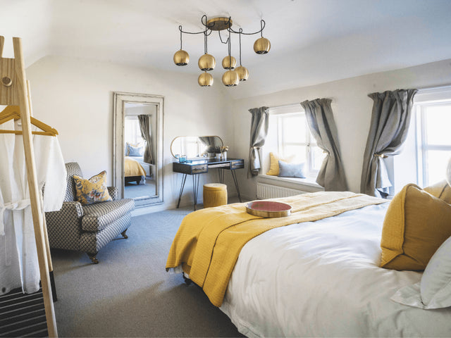 A bright bedroom decorated with warm whites, yellow and grey with an impressive brass globe cluster chandelier