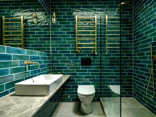 A contemporary bathroom with green tiling and brass furnishings